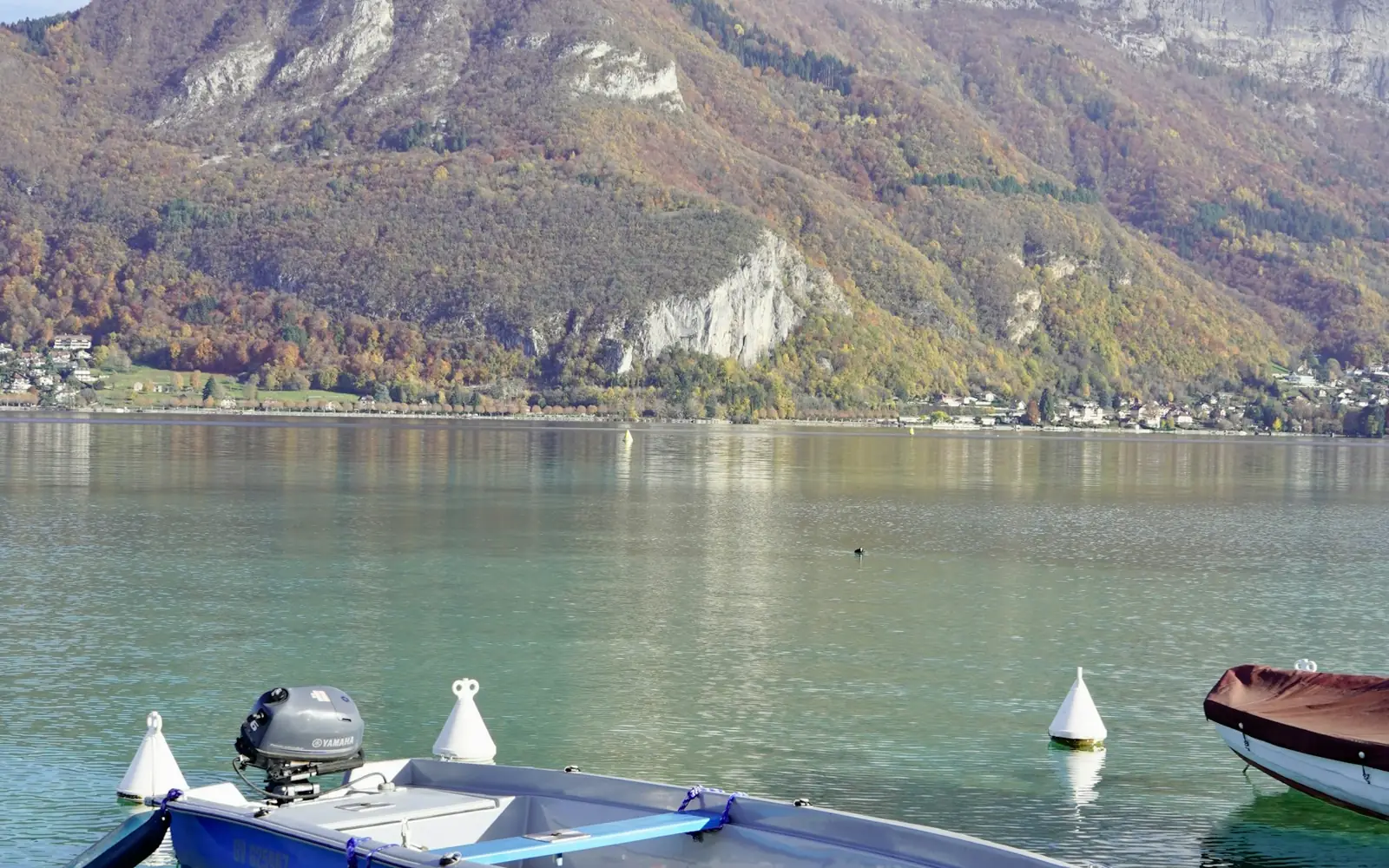 Small boats on Lake Annecy beneath wooded mountain slopes